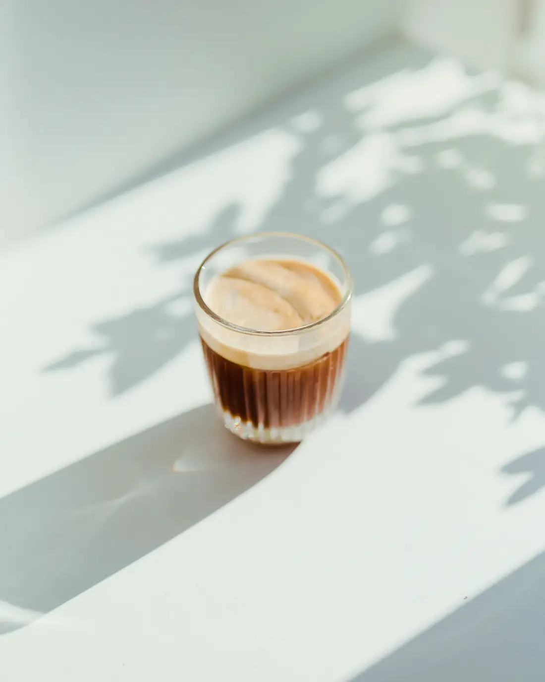 Ľadové latte v pohári na slnku s tieňmi listov