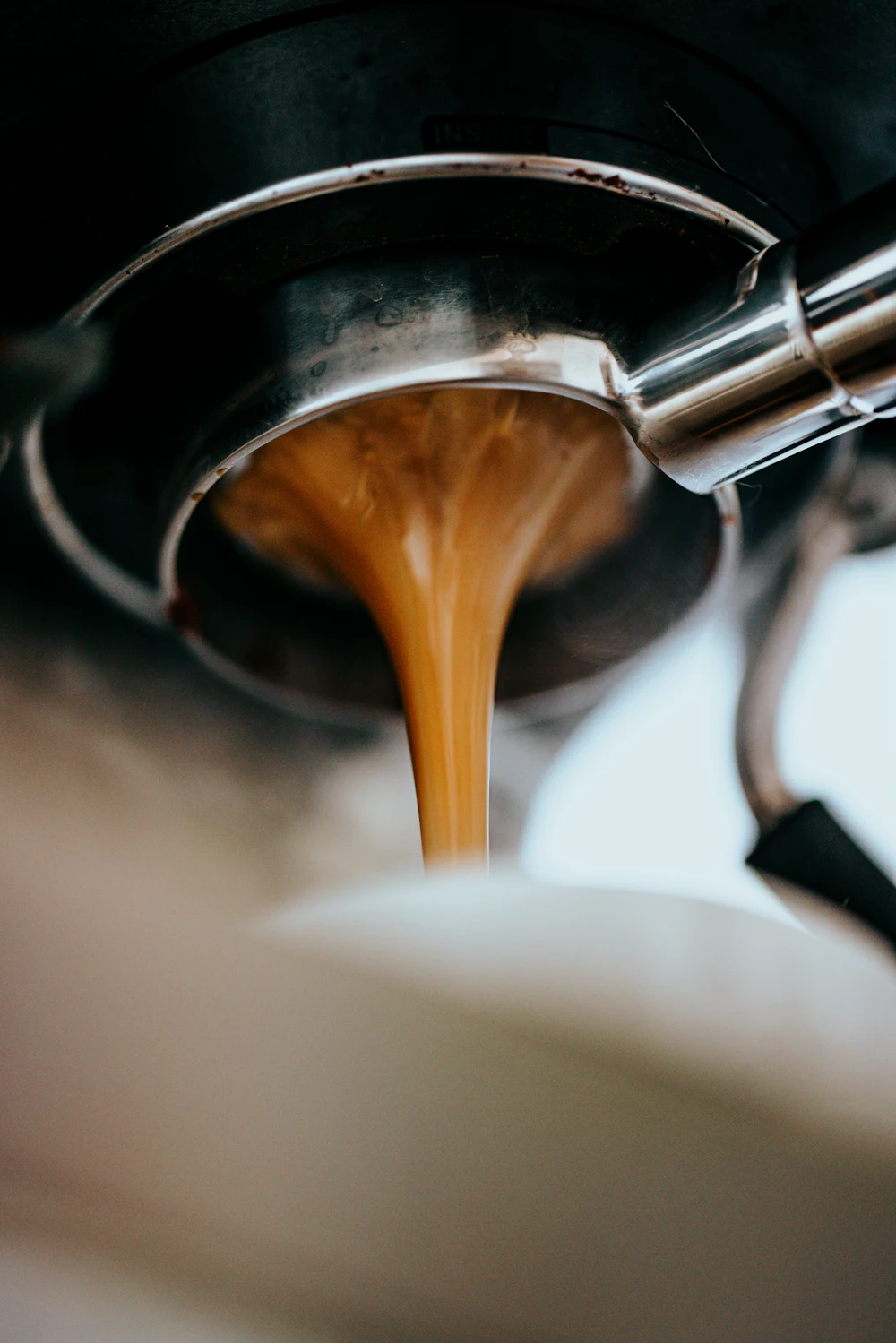 Espresso stekajúce z páky kávovaru do bielej šálky
